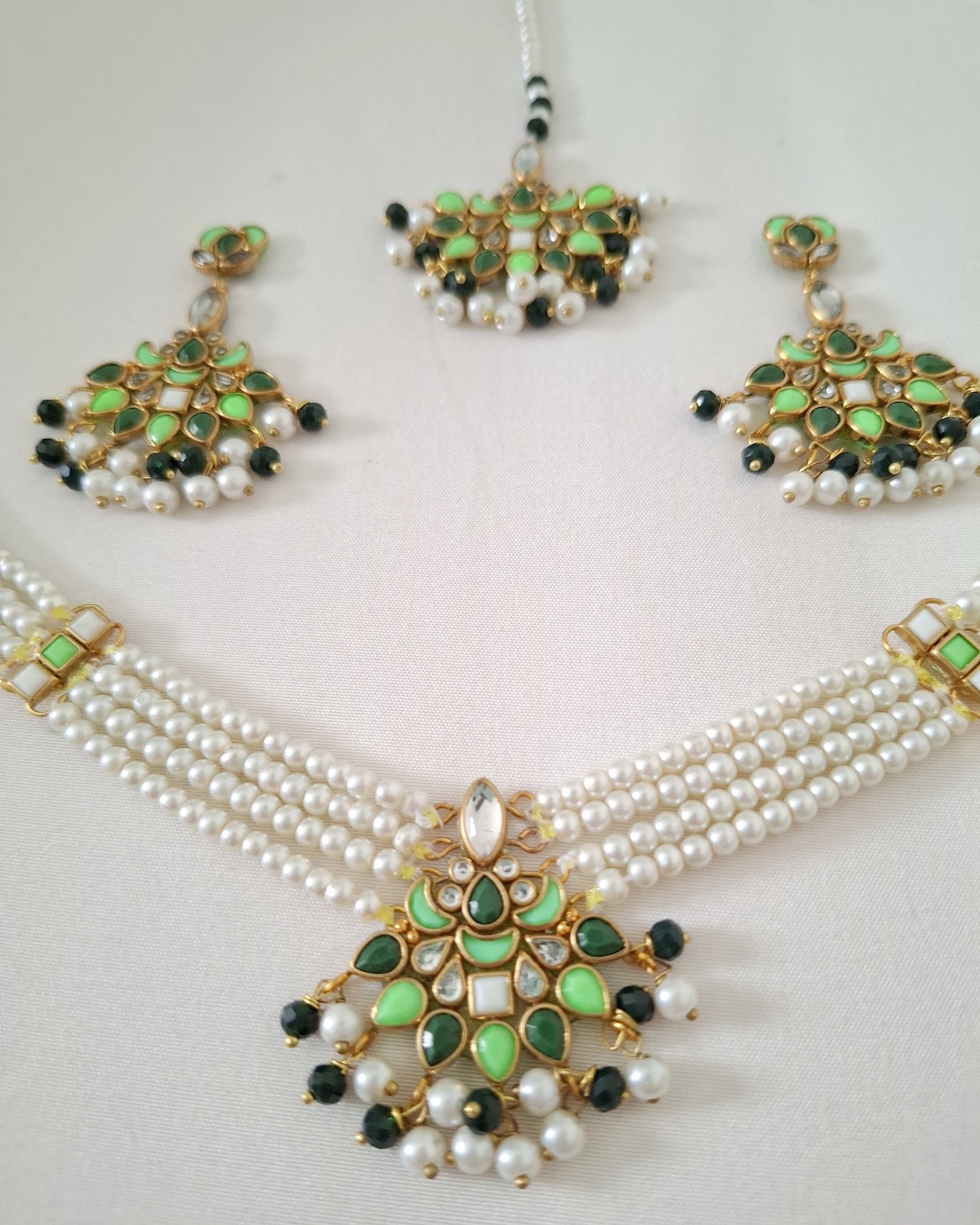 Pearl necklace with green and black embellishments on a light gray background