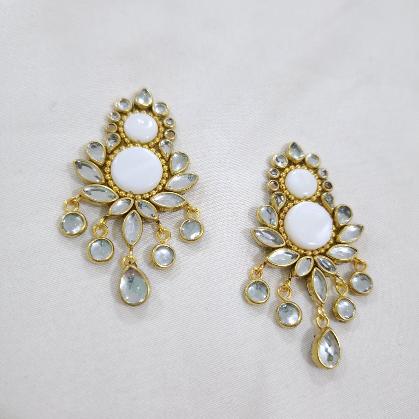 Pair of gold and white earrings on a light gray background with 'HKJ BY ZAINAB' branding.