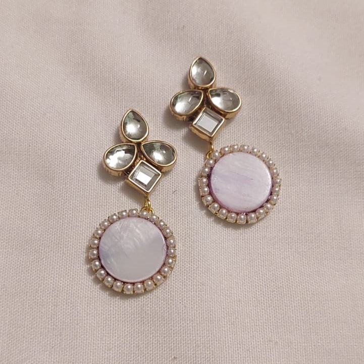 Pair of earrings with pink and white stones on a beige fabric background