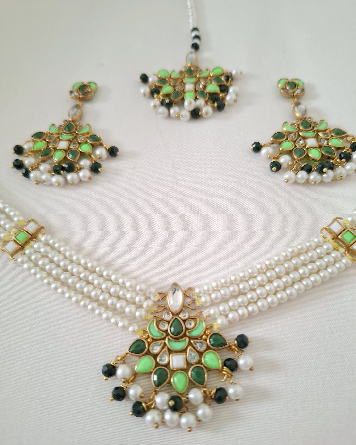 Pearl necklace with green and black embellishments on a light gray background
