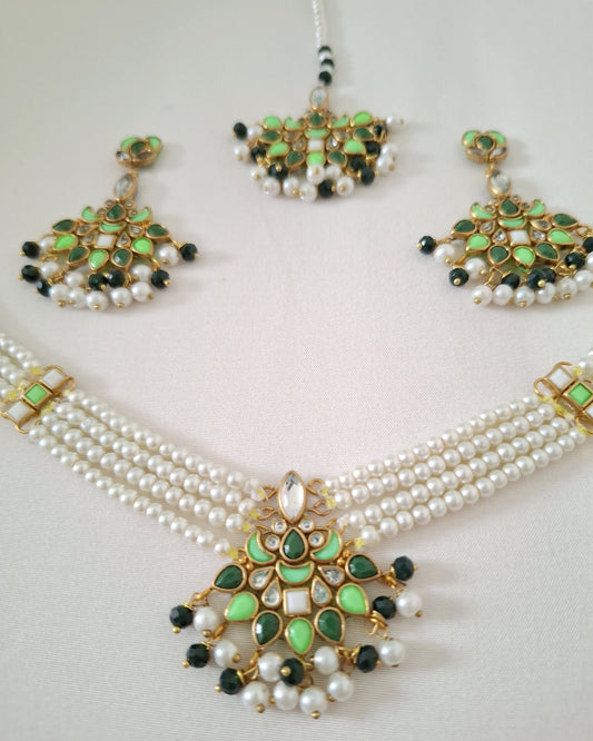 Pearl necklace with green and black embellishments on a light gray background